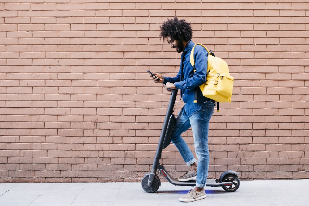 Mann med sparkesykkel ser på mobilen