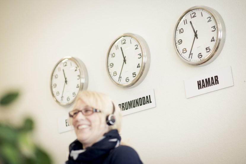 Dame med hodetelefoner sitter foran hvit vegg med klokker. foto